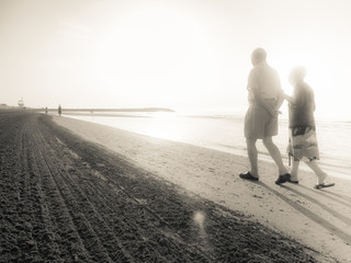 two aged people walking next to the other long the shoreline of an Italian beach in the early morning