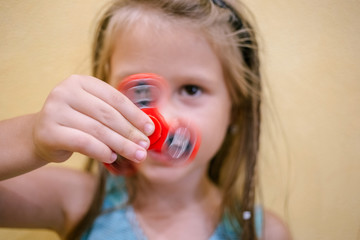 Little girl playing with red fidget spinner toy to relieve stress at home