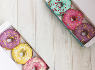 Fresh donuts with colorful glaze on the white wooden background