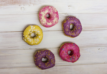 Ring of Fresh donuts with colorful glaze on the white wooden background