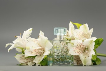 flowers white lilies on a gray background with a glass bottle of spirits.