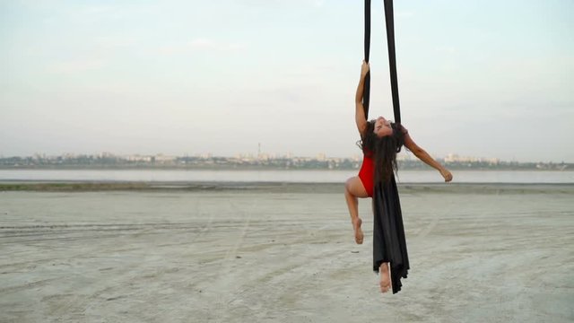 Beautiful girl dance with aerial silk on sand coast background rapid slow motion