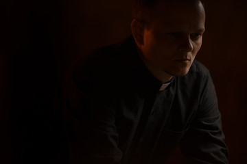 Portrait of handsome catholic priest or pastor with dog collar, dark red background.