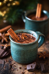 Hot chocolate with a cinnamon stick, anise star and grated chocolate topping in festive Christmas setting on dark rustic wooden background