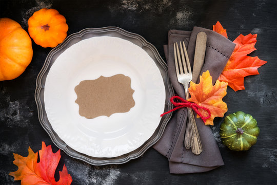 Happy Thanksgiving table place setting with vintage silverware decorated with autumnal leaves and decorative pumpkins with a plate on rustic wooden background .