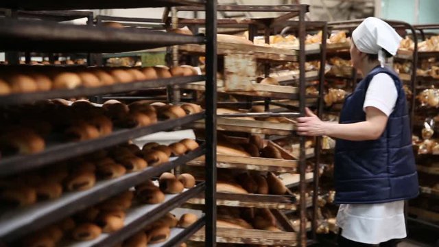 Trays with freshly baked bread at the bakery on the truck in the foreground. In the background, bakery workers in white uniforms piled bread trays. Working in a bakery. Background is blurred.