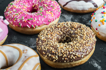 assorted doughnuts in the glaze and colorful sprinkles on a black background