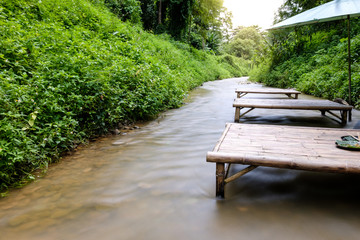 Fototapeta na wymiar Smooth water in the stream from Mae Phun Waterfalls with the local wooden chair in Laplae District, Uttaradit province of Thailand