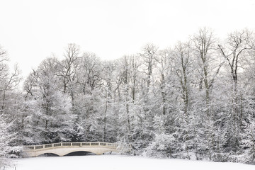 Frozen lake after snowfall on Hampstead Heath, London with bridge and trees