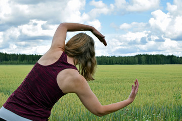 Middle aged yoga woman stretching and exercise outdoors. Rear view, field on background.