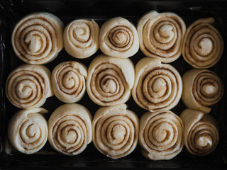 Cinnamon rolls filled with sugar, cinnamon and butter made of fresh yeast dough in black pan while rising and waiting to go in the oven