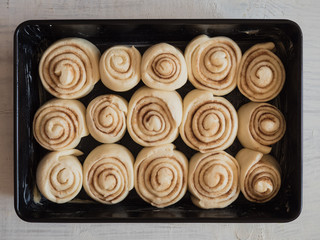 Cinnamon rolls filled with sugar, cinnamon and butter made of fresh yeast dough in black pan while rising and waiting to go in the oven