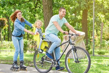 Full length shot of a happy young family enjoying cycling and rollerblading child sitting in a baby bike seat active parents sports lifestyle weekend recreation nature concept.