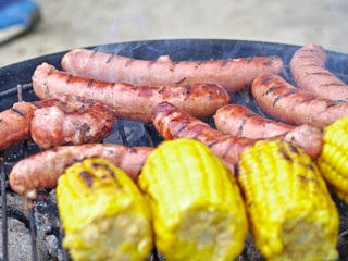 Yellow corncobs and tasty sausages on the grill.