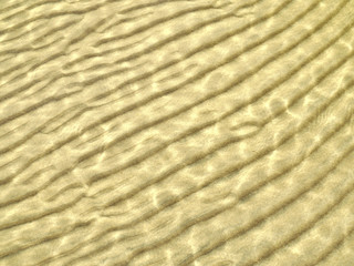 Beautiful sunlit wave pattern on the sandy sea bottom. Natural background.