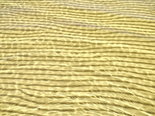 Beautiful sunlit wave pattern on the sandy sea bottom. Natural background.