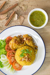 Chicken Biryani on white dish with green sauce (Muslim yellow rice with chicken) on brown wooden background