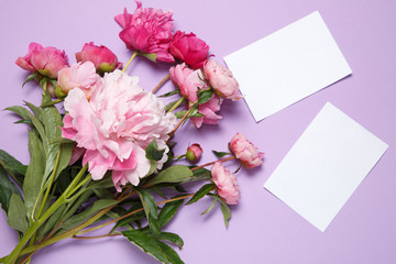 A bouquet of pink peonies and a sheet of white paper lies on a lilac background.