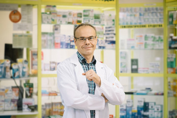 Handsome smart man in a white suit, wearing glasses standing  in his Pharmacy store