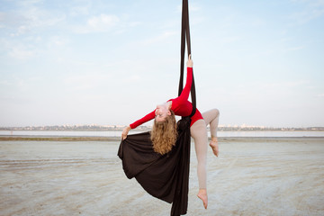 Fit woman in skinny skinny clothes dancing with aerial silk on a sky background, gymnast training...