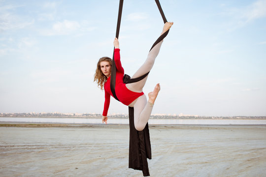 Fit woman in skinny skinny clothes dancing with aerial silk on a sky background, gymnast training on aerial silk 