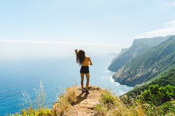 Hiker girl standing at rocks and overlooking Madeira volcano coast and ocean