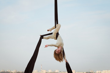 Fit woman in skinny skinny clothes dancing with aerial silk on a sky background, gymnast training...