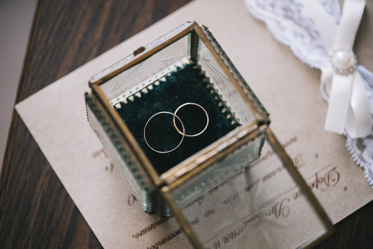 Beautiful golden wedding rings inside a vintage glass box, on the wedding invitation and wooden table background