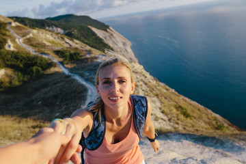 Naklejka premium man helping active young woman hiker to climb the mountain. cropped image of a man's hand helping lady tourist. Lifestyle and relationship concept