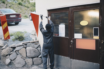 Rear view of female mechanic mounting orange flag on door of auto repair shop