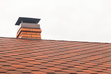 Chimney pipe in red bricks on roof in red shingles. On white background
