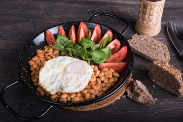 Beans, eggs, bread, tomatoes in a black frying pan