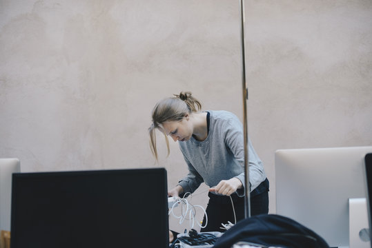 Female computer programmer fixing tangled cables against wall in office