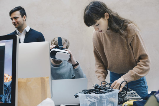 Computer programmer wearing VR glasses while colleagues working in office