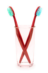 Две красные зубные щетки в стекляном стакане на изолированном белом фоне