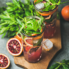 Blood orange citrus lemonade with fresh mint and ice cubes in tall glasses on wooden board over dark brown stone background, square crop. Refreshing summer drink concept