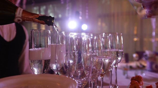 The waiter pours champagne in wineglass, in a restaurant, The waiter pours champagne in crystal glasses, Restaurant interior, buffet table, Waiter in white gloves, close-up