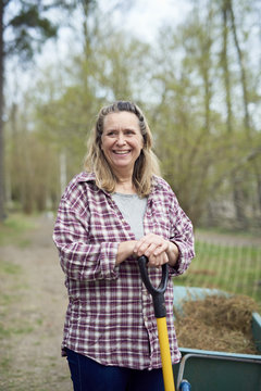 Smiling mature woman looking away while holding pitchfork on field