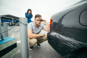 sad man looking on car scratch, woman stand behind him