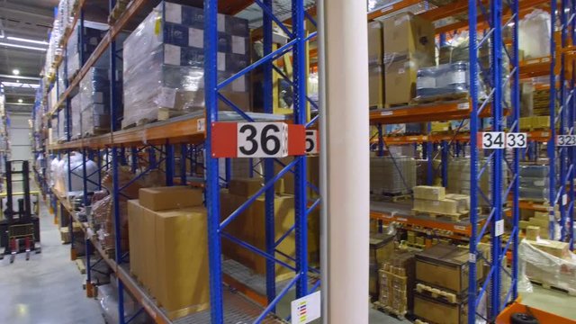Forklift trucks goes between warehouse shelves in a modern storehouse with many racks, shelves.