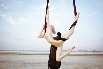 exercises with aerial silk outdoor, sky background. beautiful fit woman training acrobatic in airt. 