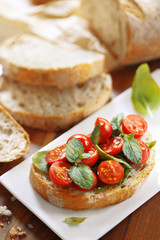 Bruschetta with tomato and basil. Bread loaf slice in a background.