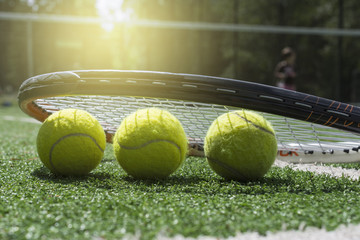 Tennis balls and racket on tennis court with artificial turf under sunlight