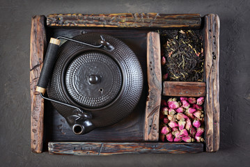 Asian black traditional teapot with dry tea and rose in vintage wooden box