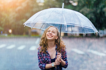 Pretty student girl in plaid shirt holding umbrella in the rain. Sun glare effect.