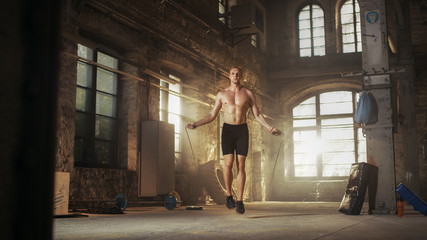 Athletic Shirtless Fit Man Exercises with Jump / Skipping Rope in a Deserted Factory Hardcore Gym. He's Covered in Sweat from His Intense Cross Fitness Training.