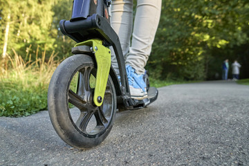 Girl riding on the kick scooter in the park in summer evening close up. Low angle view.    