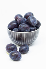 Plums in a bowl, separated, close up. White background.