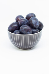 Plums in a bowl, separated, close up. White background.