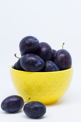 Plums in a bowl, separated, close up. White background.